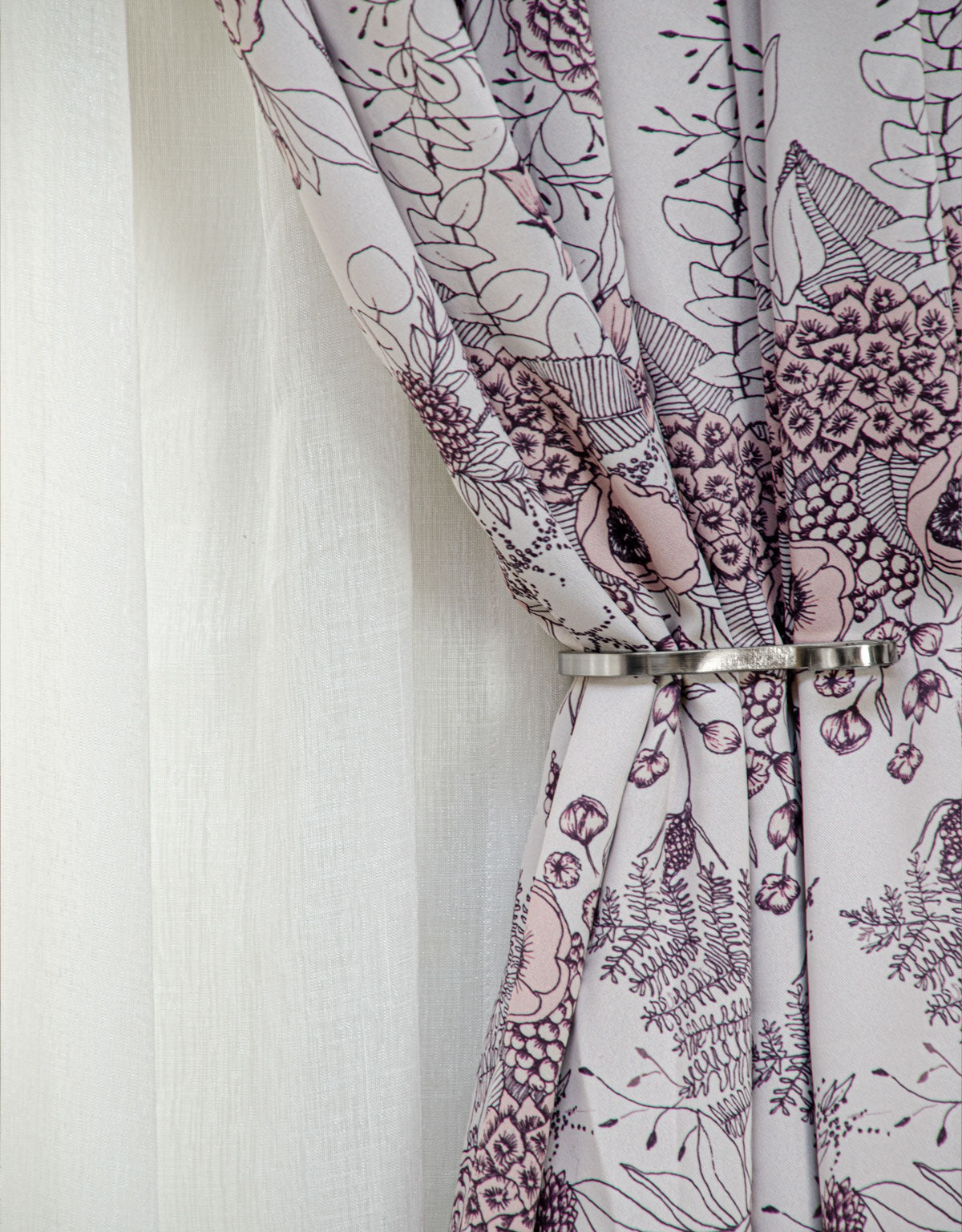 Light pink floral curtain behind a curtain tieback in steel