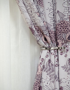 Light pink floral curtain behind a curtain tieback in steel